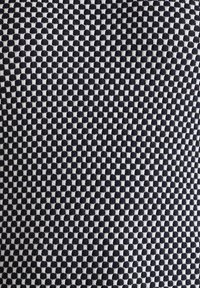 Czarnobiała tkanina w wzór z gridem na przemian pełnych i konturowych kwadratów, o miękkiej teksturze i gęstym splocie.