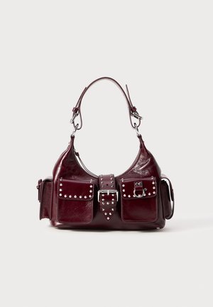 Burgunderfarbene Lederhandtasche mit geschwungenem Design, silbernen Nieten, zwei Fronttaschen und einem abnehmbaren Tragegurt für vielseitige Trageoptionen.