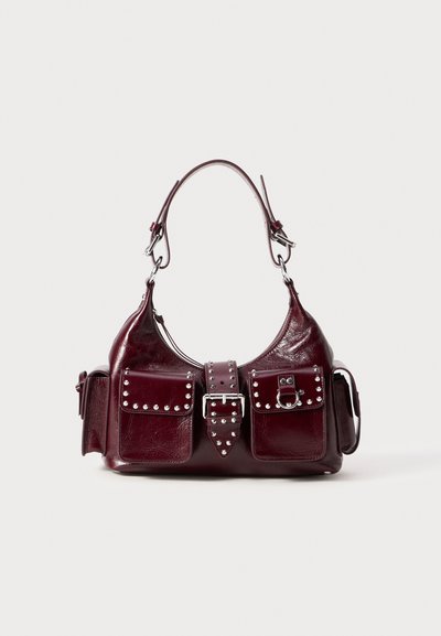 Bordeaux leren handtas met een gebogen ontwerp, zilveren studs, twee voorvakjes en een afneembare schouderband voor veelzijdige draagmogelijkheden.