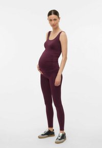 Graviditetslinne och leggings i djup burgundy, med en figurnära design och slät textur, i kombination med svarta och grå sneakers.