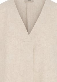 Tissu en lin beige avec un décolleté en V profond et un détail de couture subtil sous le cou sur un vêtement.