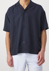Camisa de botones de manga corta en color marino, hecha de una tela ligera con cuello extendido y una textura sutil, combinada con pantalones claros de rayas.