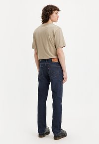 Beige short-sleeve t-shirt paired with dark blue denim jeans. Jeans feature a leather patch at the waist and standard back pocket design.