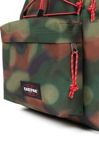 Zaino Eastpak con motivo mimetico, realizzato in tessuto testurizzato, dettagli in cordino rosso e una tasca frontale. Presenta una patch con il logo sul lato.