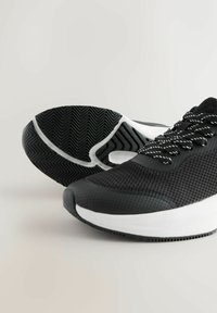 Mustad sportjalatsid tekstuuriga võrgus ülaosaga, valgete aktsentidega keskplatvormil ja mustrilise kummist välispõhjaga haarduvuse tagamiseks.