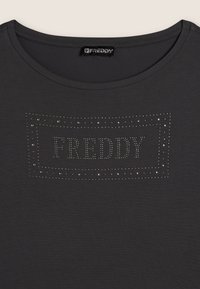 Camiseta gris oscuro con cuello redondo, que presenta un diseño rectangular de strass que dice "FREDDY" en el centro. Textura suave.