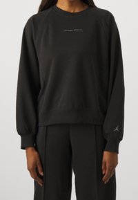 Felpa nera realizzata in tessuto morbido, con collo a giro, maniche raglan e un piccolo logo bianco "Jordan Sport" sul petto.