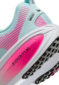 Light blue athletic shoe with pink accents, featuring a textured upper and a cushioned sole, labeled "zoomx" in black.
