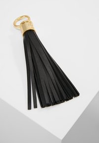 Black leather keychain tassel with thin, elongated strips and a gold metal ring at the top. Textured surface detail visible.
