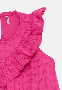 Rosa bomullsbluse med blomsterbroderi, bølgete utringning og kortermede med scallopkanter.