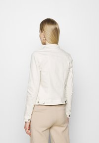 Giacca di jeans beige con un design aderente, polsini abbottonati e dettagli in metallo. Presenta un colletto classico e un particolare retro con yoke.