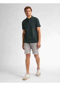 Donkergroen poloshirt met twee knopen, gecombineerd met lichtgrijze denim shorts met opgerolde zoom. Witte sneakers met beige accenten.