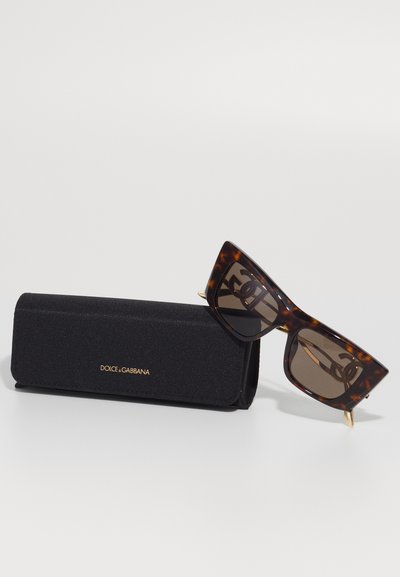 Tortoiseshell cat-eye sunglasses with brown lenses leaning on a black Dolce & Gabbana hard case with gold logo.
