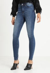 Jeans ajustados azul oscuro de mezclilla, con cintura alta y un ligero desvanecimiento. Combinados con mule negros con tacón transparente.