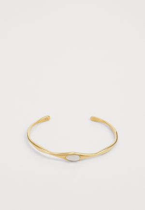 Złoty metalowy bransoletka z gładkim, zaokrąglonym wzorem i owalnym białym kamieniem akcentującym na środku. Polerowane wykończenie, minimalistyczny styl.
