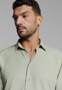Lichtgroen, kortmouw overhemd van gestructureerde stof. Beschikt over een knoopsluiting aan de voorkant, een zacht kraagje en een subtiele merklogo op de borst.