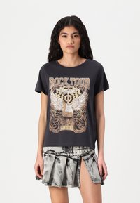 T-shirt graphique noir avec un design "Rock Tour", à manches courtes et coupe décontractée. Associé à une jupe en denim plissée, délavée, de couleur grise.