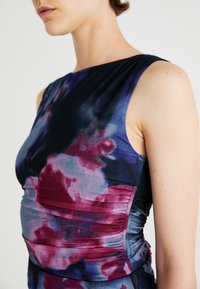 Haljina bez rukava od rastezljivog materijala, s višebojnim tie-dye uzorkom u nijansama ljubičaste, plave i crvene boje, s nabranim detaljima.