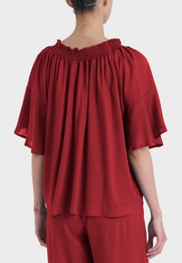 Top rosso a maniche corte con scollatura arricciata. Tessuto fluido che crea una vestibilità rilassata. Design minimalista con una texture liscia.