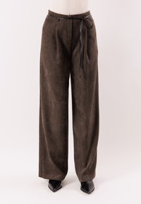 Pantaloni marroni a gamba larga in tessuto strutturato, con cintura a coulisse e pieghe frontali, abbinati a scarpe nere con punta a punta.