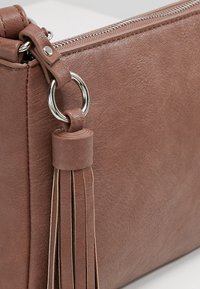 Brun læderclutch med en struktureret overflade, der har en sølvlynlås, en ringophæng og en frynse detalje.