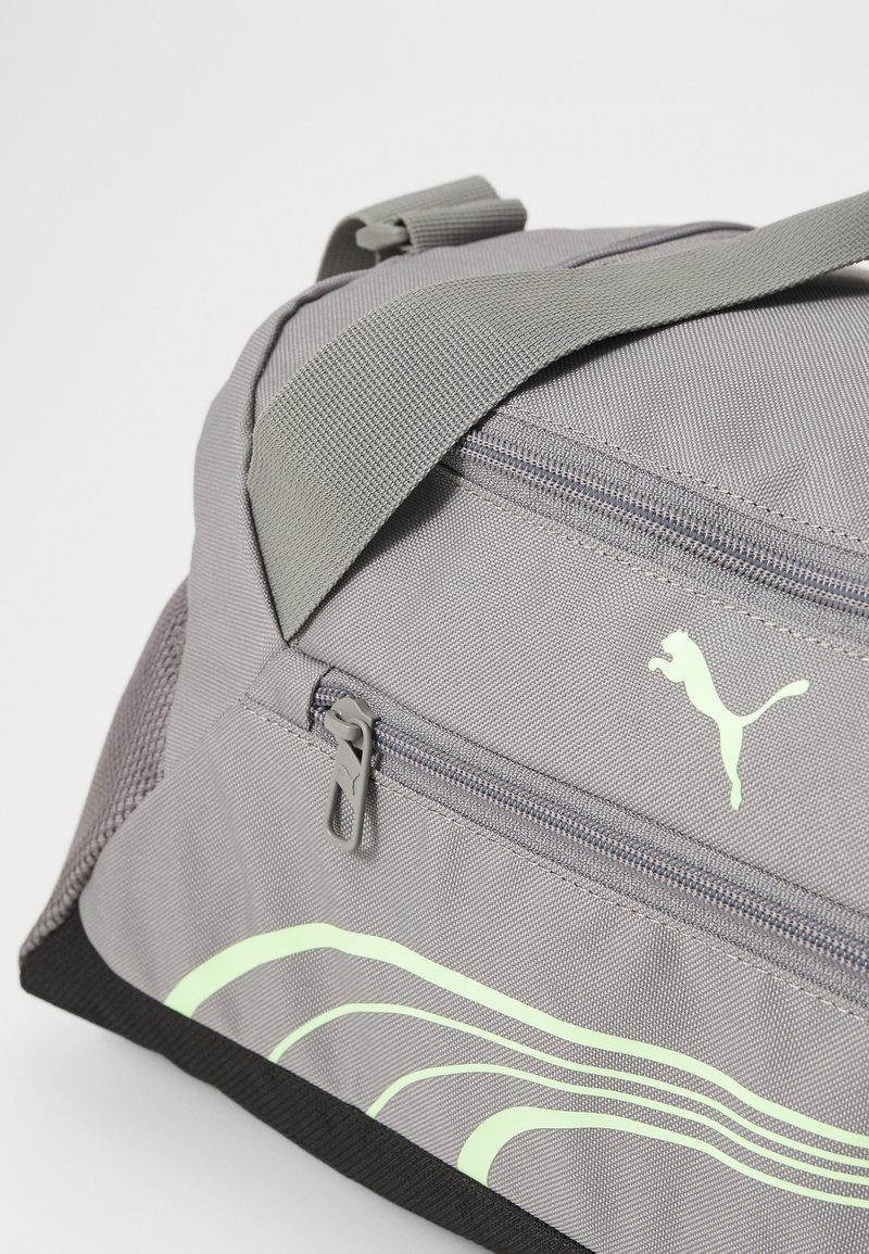 Grau duffel bag mit glatter Textur, ausgestattet mit einer Reißverschlusstasche, reflektierenden grünen Akzentlinien und einem kleinen Logo. Robustes Material und verstellbarer Gurt.