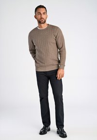 Ljusbrun kabelstickad tröja med rundad hals, i kombination med mörk marinblå byxor och svarta lackskor. Slät textur och figursydd design.