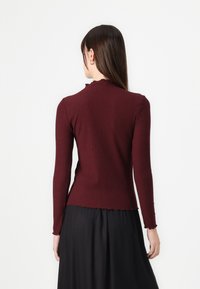 Burgundy långärmad ribbad topp med en åtsittande design, scallopat halsringning och fåll. Slät textur och minimalistisk stil.