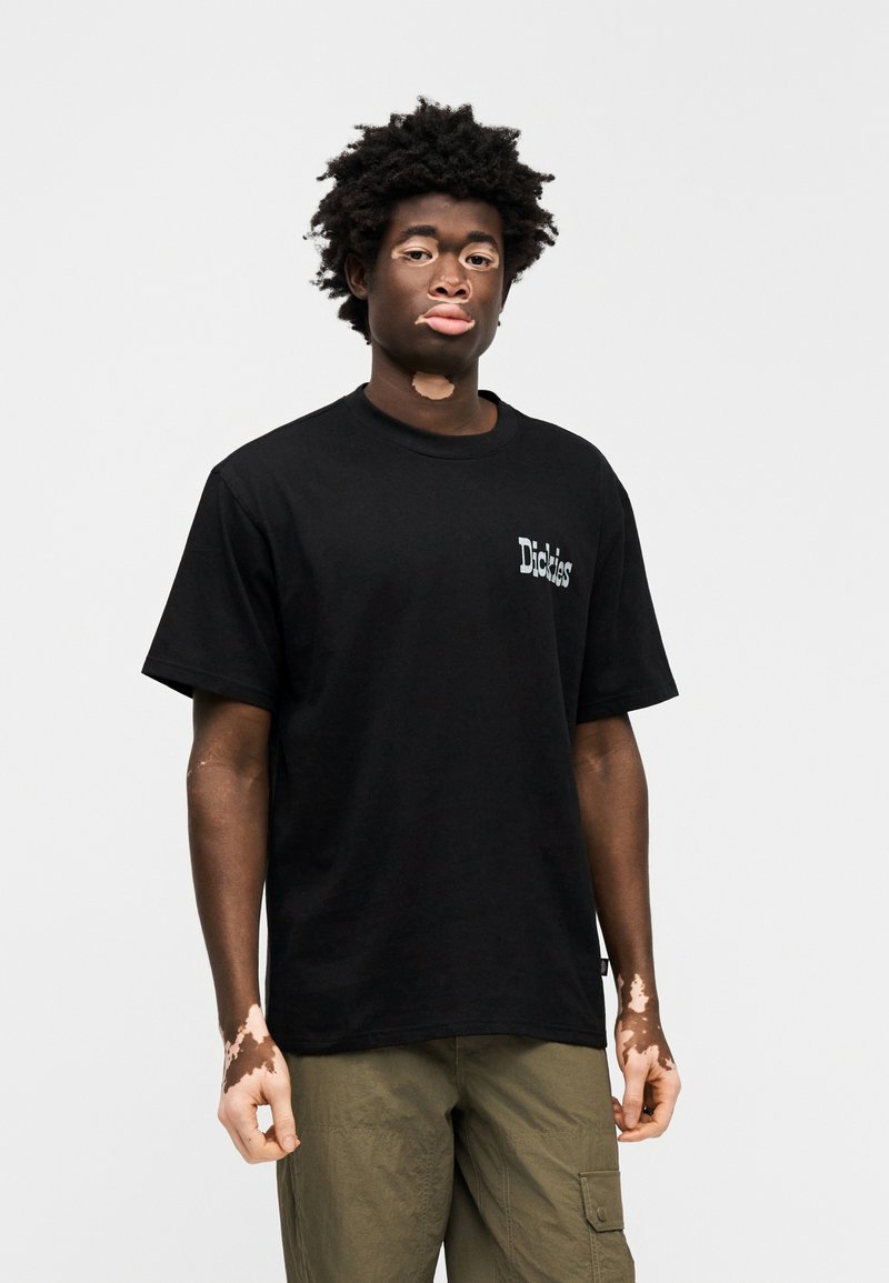 Black cotton t-shirt with a round neck and short sleeves, featuring white text branding on the chest. Paired with olive green cargo pants.