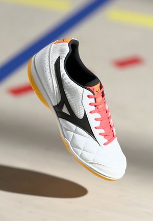 White athletic shoe with a quilted pattern, black accents, and bright pink laces. Yellow sole, synthetic material with textured detailing.