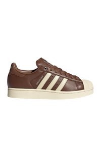 Καφέ δερμάτινο αθλητικό παπούτσι Adidas Superstar με εκρού μύτη παπουτσιού, σόλα και τρεις πλευρικές ρίγες, σε προβολή από την εξωτερική πλευρά.
