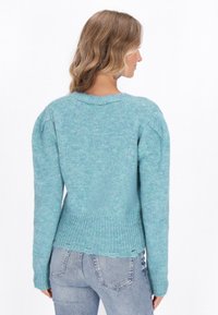 Svetlo modrý pletený sveter s textúrovaným povrchom, dlhými rukávmi, okrúhlym výstrihom a elastickým rebrovaným lemom. Nosený s džínami strednej umývanej farby.