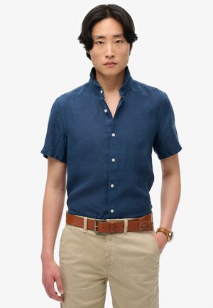 Camisa de botones de manga corta en color navy, hecha de lino con cuello alto. Cuenta con botones blancos y una textura suave, combinada con pantalones caqui.
