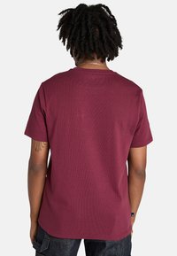 Mörkröd t-shirt med kort ärm och rund hals, med en slät textur och avslappnad passform. Bakifrån syns en ren design utan grafik.