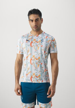Camiseta deportiva de manga corta en gris claro con patrones geométricos abstractos en naranja y teal. Presenta detalles de logo en el pecho.