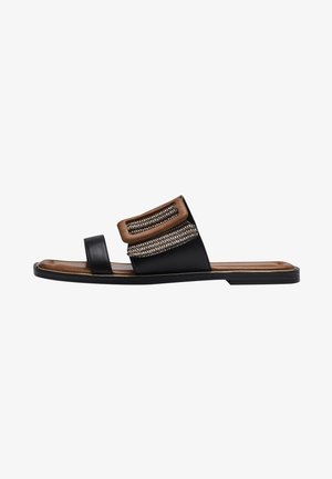 Infradito in pelle nera con una fascia accentuata marrone testurizzata che presenta dettagli intrecciati; suola piatta con una finitura in legno sotto.
