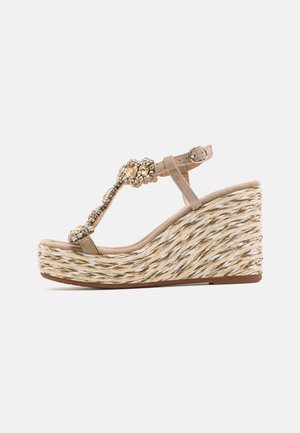 Beige wedge sandals with a woven straw base, embellished with jewels on the T-strap design, featuring an adjustable ankle buckle.