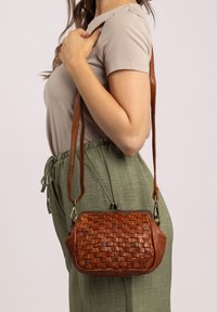 Sac bandoulière en cuir tressé marron avec une forme arrondie et une sangle amovible. Comprend des détails en rivets et une fermeture à clip.