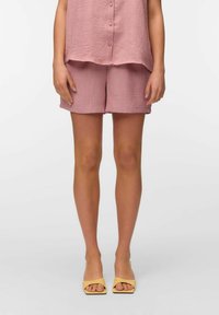 Top de lino texturizado rosa y pantalones cortos a juego, con un ajuste holgado. Combinado con sandalias amarillas de punta abierta para un acento contrastante.