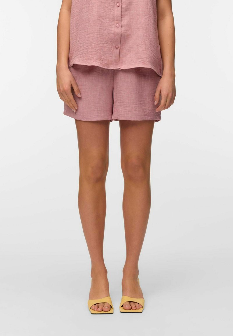 Top de lino texturizado rosa y pantalones cortos a juego, con un ajuste holgado. Combinado con sandalias amarillas de punta abierta para un acento contrastante.