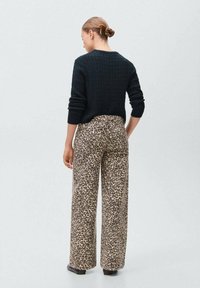 Maglione nero a maglia con un motivo testurizzato, abbinato a pantaloni a gamba larga con stampa leopardata. L'outfit presenta tonalità neutre e una vestibilità comoda.