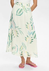 Blumenfalten-Midirock in hellem Creme, mit grünen und rosa Blattmustern. Elastischer Bund, kombiniert mit rosa Flip-Flops.