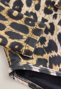 Tissu à imprimé léopard avec des motifs noirs et dorés. Texture lisse avec des coutures ajustées et une doublure noire visible sur les bords.