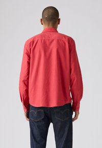 Rode overhemd met lange mouwen en een afgeronde zoom, met knopen bij de manchetten en een gladde textuur, gecombineerd met donkerblauwe denim jeans met contrasterende steken.