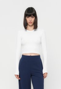Witte lange mouwen cropped top met een ronde halslijn en ribbelstructuur, gecombineerd met marineblauwe hoge taille broeken. Eenvoudig en aansluitend ontwerp.