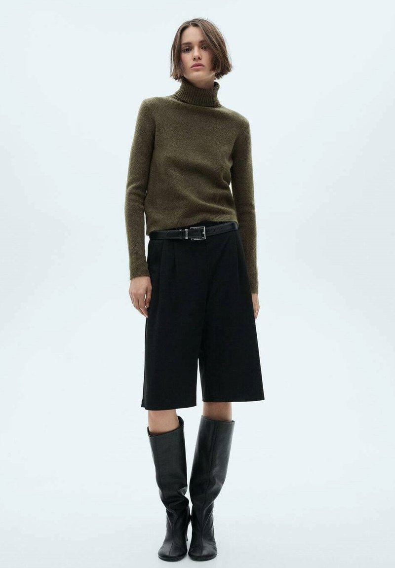Olijfgroene coltrui, zwarte high-waisted wijde shorts en zwarte kniehoge laarzen. Gladde textuur en getailleerd ontwerp.