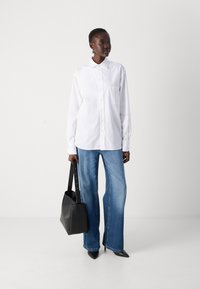 White long-sleeve shirt with a button-down collar, paired with light blue wide-leg jeans. Black handbag with a shoulder strap and pointed heels.