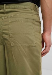 Pantalones de algodón verde olivo con un bolsillo trasero con detalle de costura cuadrada. Textura suave y diseño de pierna recta.