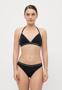 Melna bikini ar trīsstūra augšdaļu un biksītēm, kas rotāta ar kontrastējošu baltu joslu ar "EA7" logo priekšpusē. Gluda tekstūra, minimāls dizains.