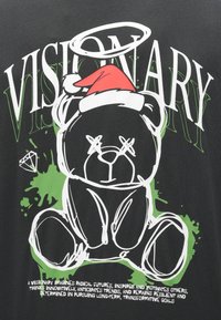 Tricou negru cu o grafică reprezentând un urs purtând o căciulă roșie de Moș Crăciun, pete de vopsea verzi și litere mari albe cu textul "VISIONARY".
